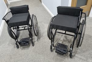 Two brand new RMA sport Fencing club wheelchairs side by side, they are sleek black with the classic open side and single side handle of fencing wheelchairs. 